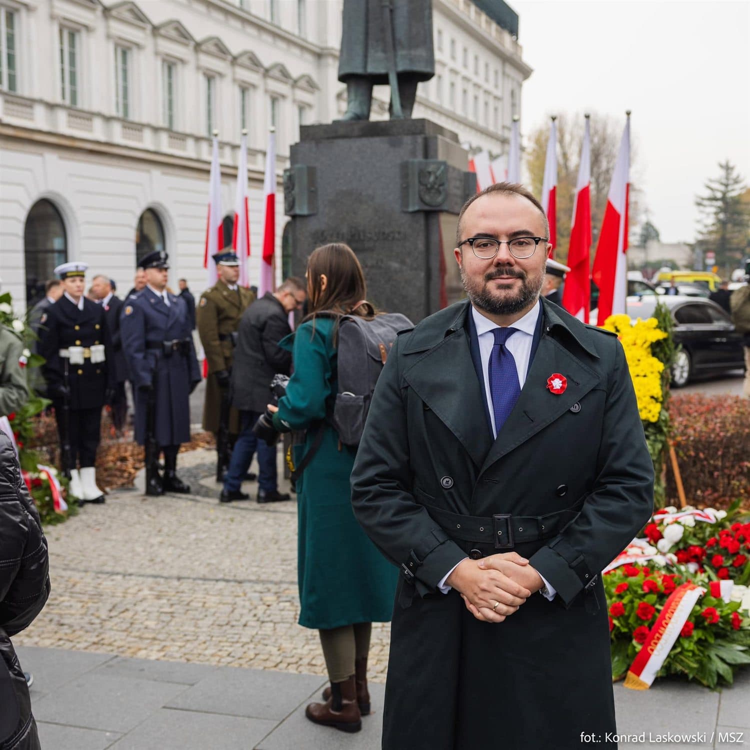 Paweł Jabłoński z biało-czerwonym kotylionem podczas obchodów Święta Niepodległości, w tle kompanie honorowe i flagi
