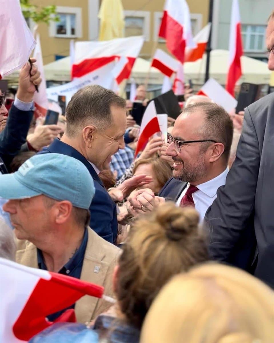 Paweł Jabłoński ściska dłoń Prezydenta RP wśród mieszkańców z biało-czerwonymi flagami podczas kampanii wyborczej